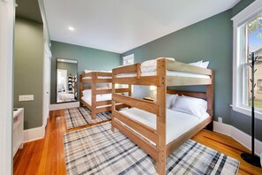 A room with bunk beds, a mirror, a window, and a plaid rug.