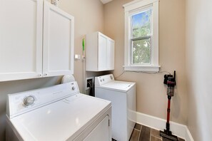 A laundry room with a front-loading washer and dryer, a window, and a vacuum cleaner.