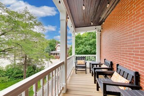 A covered outdoor deck with wooden benches and a brick wall. - The Reunion House: Two Massive Units in One! (Michigan City)