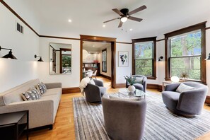 A modern living room with a sofa, armchairs, a coffee table, and a ceiling fan. - The Reunion House: Two Massive Units in One! (Michigan City)