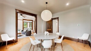 Un coin repas avec une table ronde, des chaises blanches, un luminaire suspendu et une vue sur un salon doté d’un ventilateur de plafond.