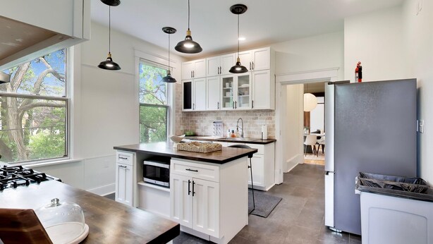 Une cuisine moderne avec des meubles blancs, une cuisinière à gaz et des luminaires suspendus.