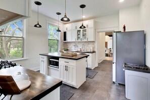 A modern kitchen with white cabinetry, a gas stove, and pendant lighting.