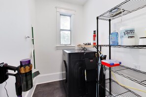 A laundry room with a washing machine, a dryer, and shelves with cleaning supplies.