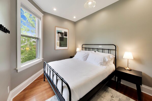 A bedroom with a bed, a nightstand, a window, and a framed picture on the wall.