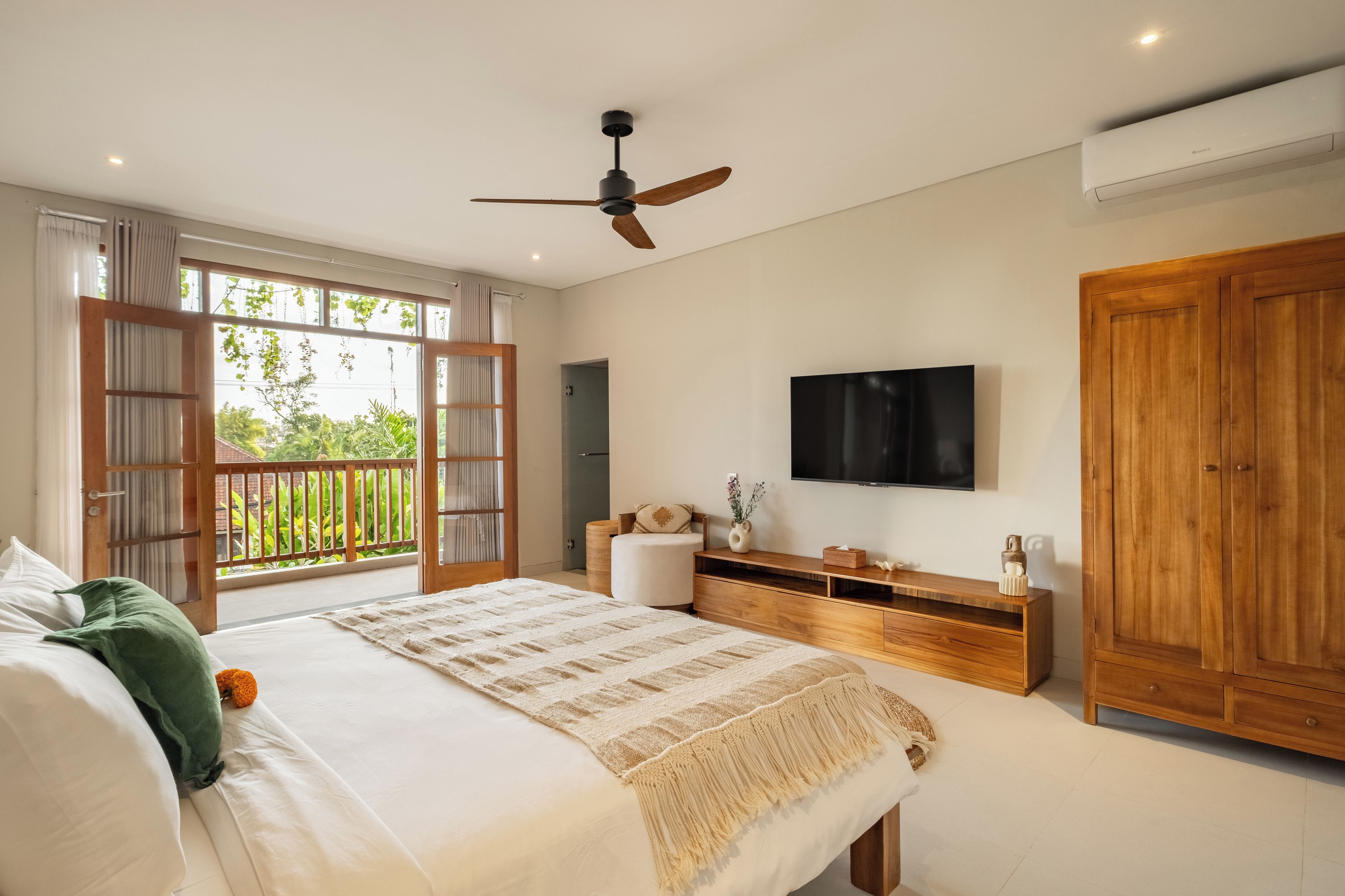 A bedroom with a bed, a TV, a wooden wardrobe, and a balcony with curtains.