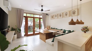A modern kitchen with a central island, a dining area with a sofa, and a TV on the left. - Villa Reviva by Villa Finder (Seminyak)