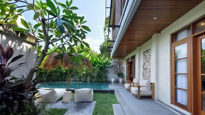 A poolside area with a thatched umbrella, white cushioned seating, and a stone wall. - Villa Reviva by Villa Finder (Seminyak)