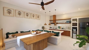 A modern kitchen with a central island, dining area with green cushions, and a ceiling fan. - Villa Reviva by Villa Finder (Seminyak)