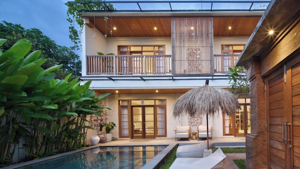 A modern two-story house with a swimming pool, a balcony with a railing, and a large umbrella. - Villa Reviva by Villa Finder (Seminyak)