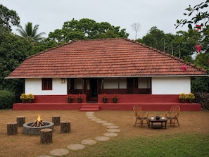 A house with a red-tiled roof, a front porch with steps, potted plants, a fire pit, and outdoor furniture.