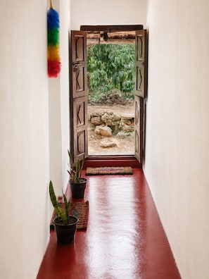 Passadís amb un paviment vermell que condueix a una porta de fusta oberta amb vista a un jardí.