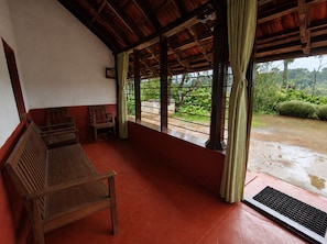 A covered porch with wooden benches, a tiled floor, and a view of greenery outside.