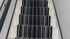 Uma escadaria com carpete listrado, corrimão e um quadro na parede.