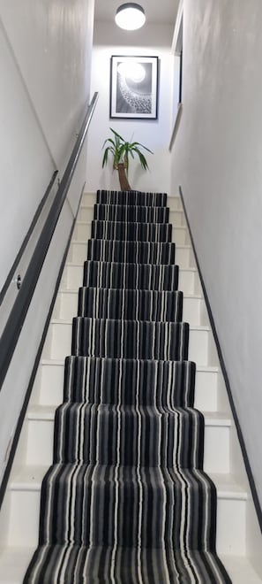 A staircase with striped carpet, a handrail, and a framed picture on the wall.