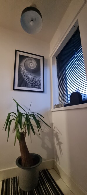 A framed artwork of a spiral staircase, a potted plant, and a window with blinds.