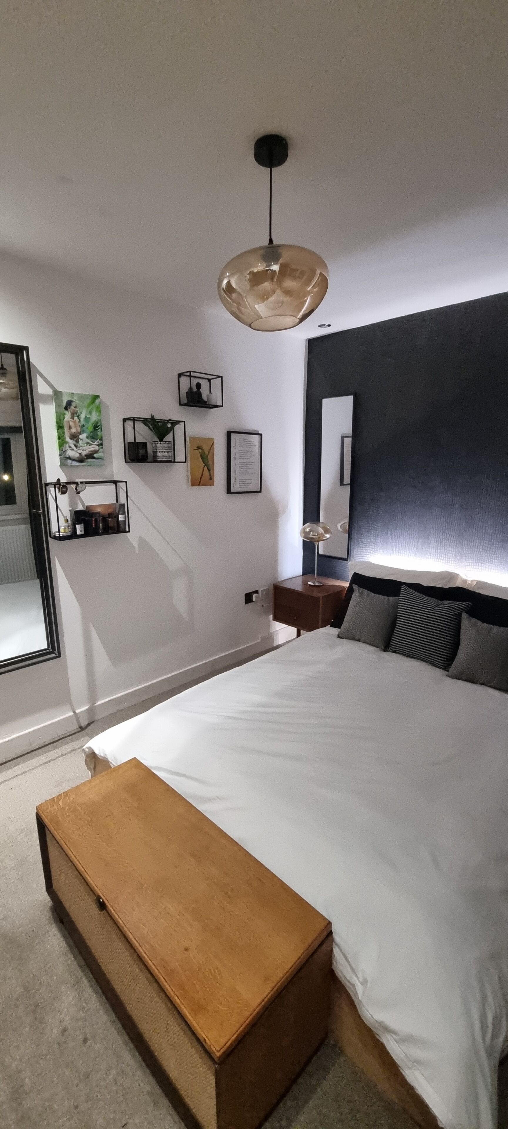 A bedroom with a large bed, a wooden bench, a bedside table, a mirror, and wall art.. Stylish and Modern One-Bed Apartment. Weekly/Monthly/Contractor Rates available.