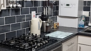 Uma cozinha com fogão a gás, forno, micro-ondas e panelas penduradas.