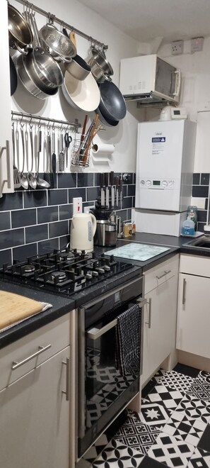 A kitchen with a gas stove, oven, microwave, and hanging pots.