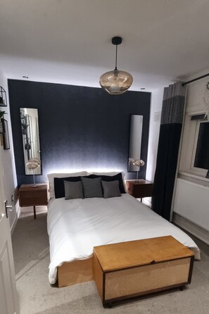 A bedroom with a bed, bedside tables, a hanging light fixture, a mirror, and a window with curtains.