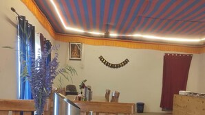 Zona pranzo con tavoli e sedie di legno, un vaso con fiori e un soffitto a righe.