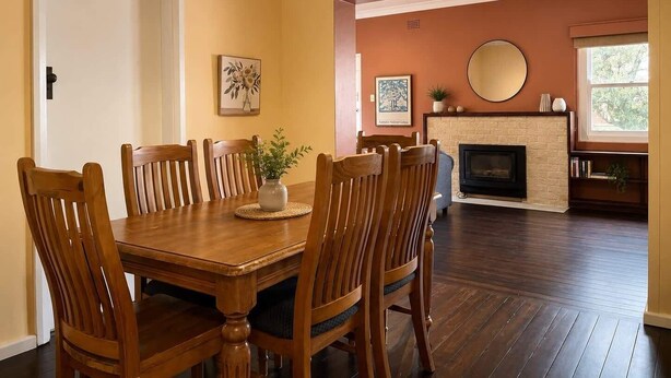 A dining room with a wooden table and chairs, a fireplace, and a large window. - Nandi - Vintage Character (Orange)