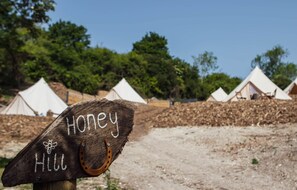A wooden sign with 'Honey Hill' written on it, surrounded by tents and trees.