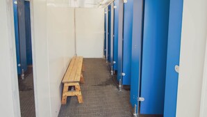 Un couloir avec des casiers bleus, un banc en bois et un sol carrelé.