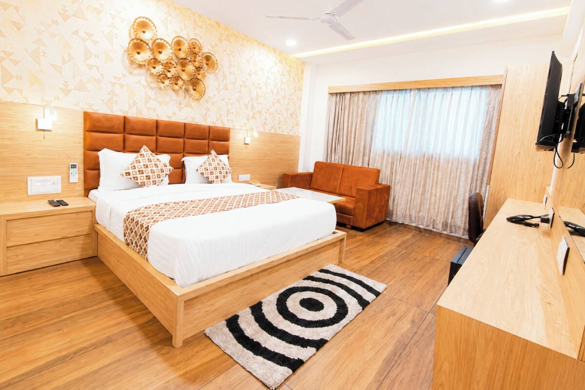 A modern hotel room with a wooden bed, a desk, a chair, a ceiling fan, and a large window with curtains.
