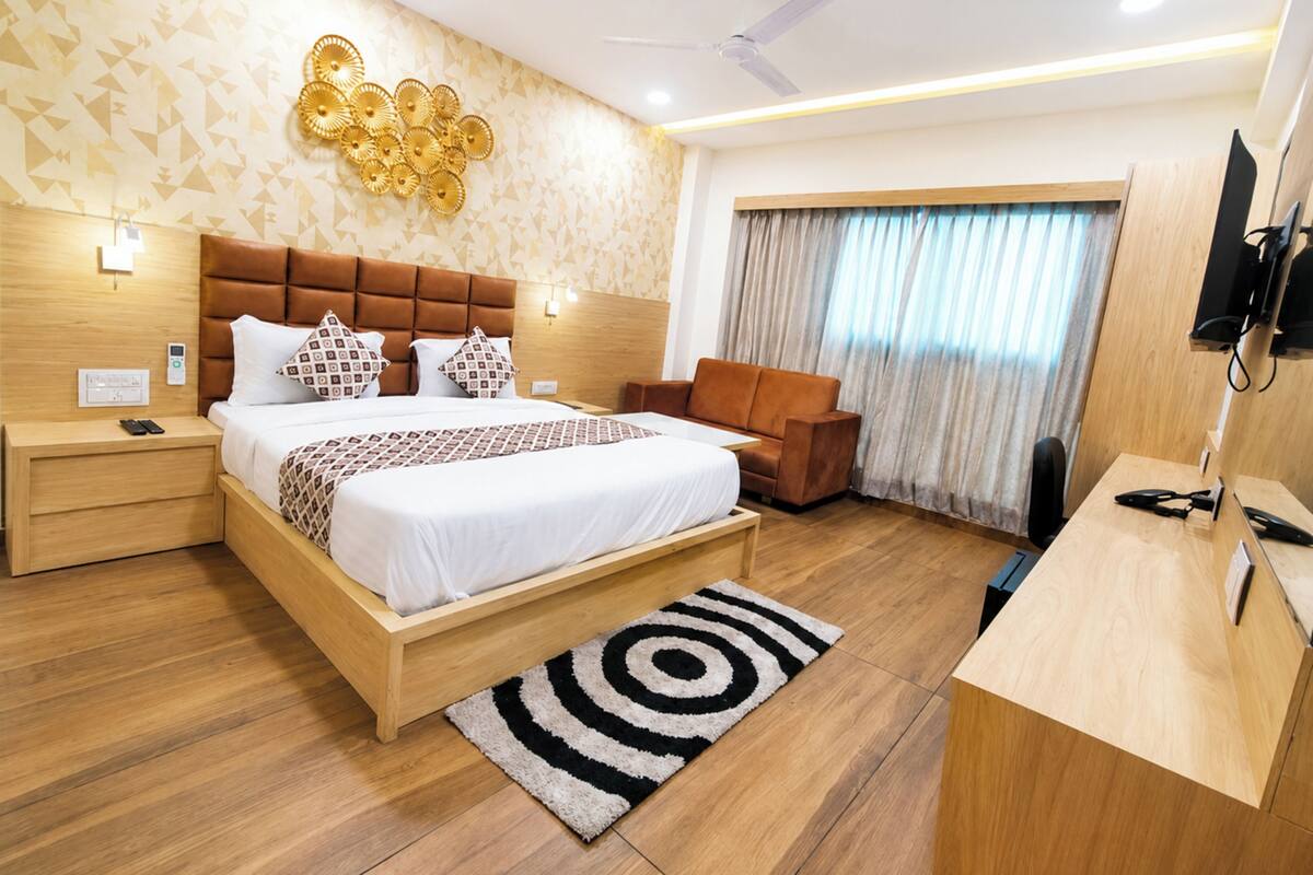 A modern hotel room with a large bed, a desk, a chair, a ceiling fan, and a TV.