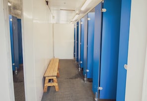 A hallway with blue lockers, a wooden bench, and a tiled floor.