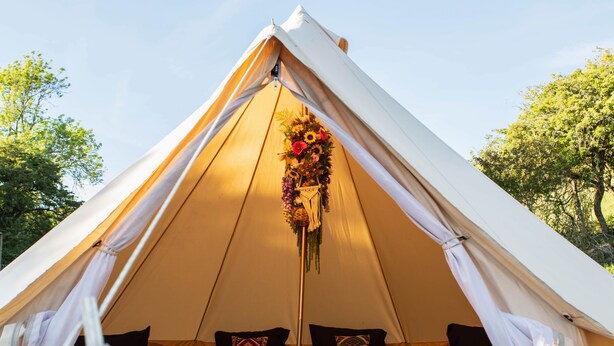 Una tenda con un letto all'interno, una decorazione appesa e alberi sullo sfondo.