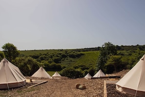 A series of tents set up in a natural landscape with rolling hills and trees in the background.
