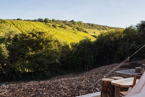 A campsite with a view of a green hillside, wooden benches, and a tent.