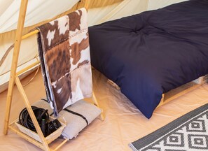 A tent with a bed, a sleeping bag, and a charging station with cables. - Bloom Canyon luxury bell tent glamping (Alfriston)