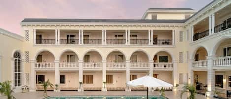A hotel with a pool, outdoor seating, and a multi-story building with balconies.
