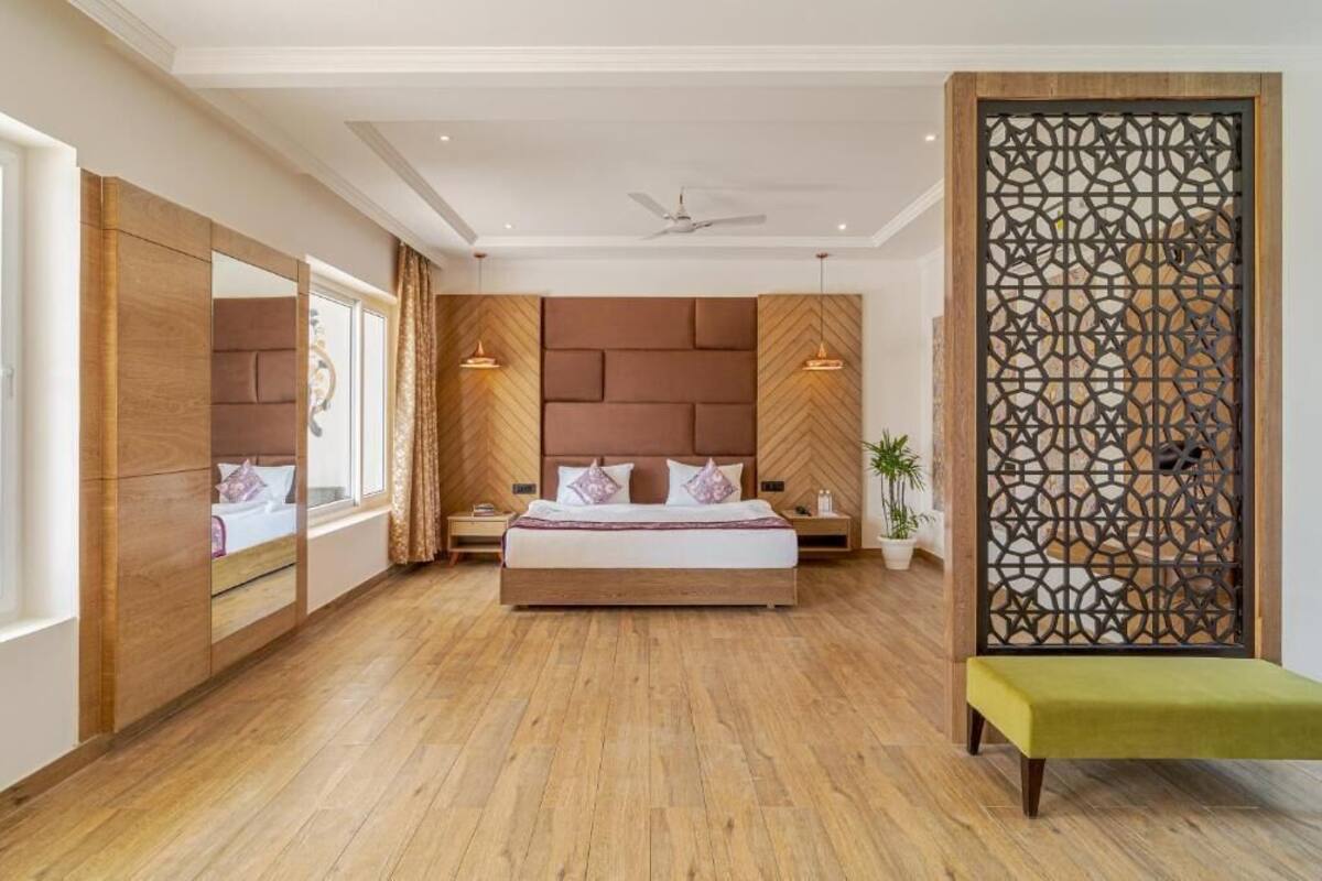 Un dormitorio con una cama grande, cabecera de madera, un biombo decorativo y una banca.