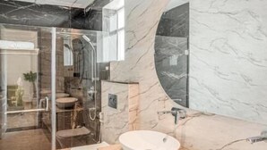 A modern bathroom with two sinks, a glass shower enclosure, and a marble wall. - Rudra Imperial Resort (Sitapur)