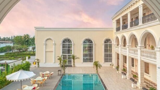 A poolside view with a balcony, a pool, and a building with arched windows and balconies. - Rudra Imperial Resort (Sitapur)