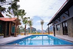 A swimming pool with a stone building and palm trees in the background. - Laco green Trang An (Hoa Lu)