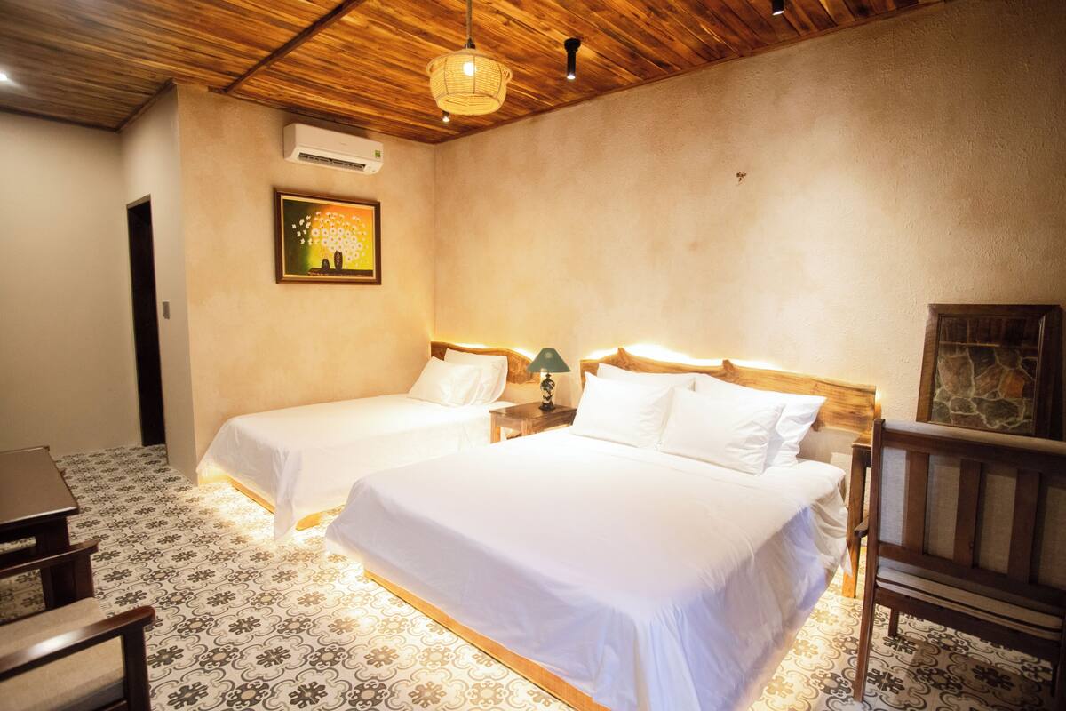 Habitación de hotel con dos camas, techo de madera, suelo estampado y un cuadro en la pared.