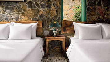 A hotel room with two beds, a nightstand with a lamp, and a stone wall.