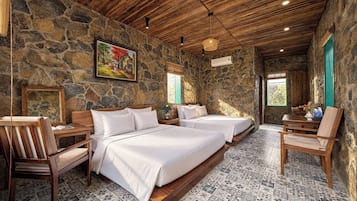 A room with a stone wall, wooden ceiling, two beds, a chair, a table, and a painting.