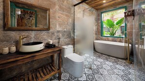 A bathroom with a stone wall, a wooden vanity, a sink, a toilet, and a bathtub.
