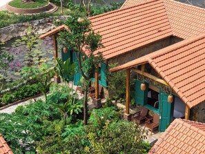 A traditional building with a tiled roof, surrounded by lush greenery and a pond with lotus flowers. - Laco green Trang An (Tay Hoa Lu)