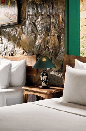 A room with a stone wall, a wooden nightstand, a lamp, and white bedding. - Laco green Trang An (Tay Hoa Lu)