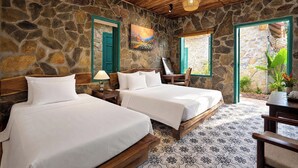 A room with stone walls, wooden ceiling, two beds, a chair, and a painting.