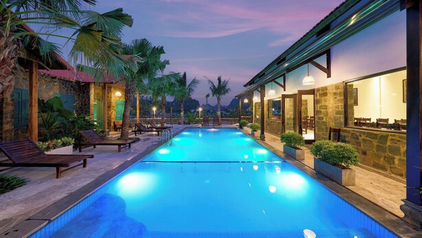 A swimming pool with lounge chairs and a stone building with a red roof.