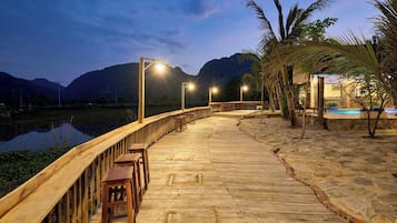 Una terraza de madera con bancos, un sendero de piedra y un cuerpo de agua al fondo.
