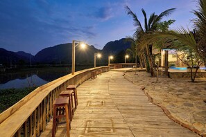 A wooden deck with benches, a stone pathway, and a body of water in the background. - Laco green Trang An (Tay Hoa Lu)